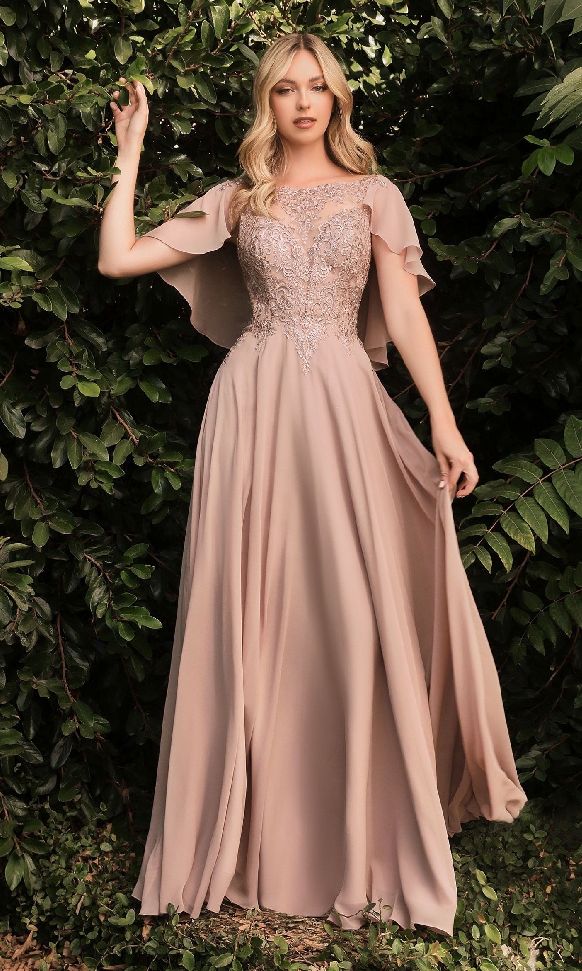 A woman stands before lush green foliage, wearing the Ladivine HT101 Cape-Sleeve Long A-Line Prom Dress in blush pink with lace details.